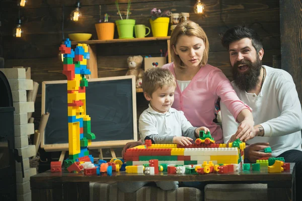 Concepto de sala de juegos. Niño pequeño jugar con ladrillos de juguete en la sala de juegos. Hijo con madre y padre construyen modelo de estructura en sala de juegos. Divertirse en la sala de juegos — Foto de Stock