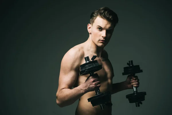 Work out concept. Man with torso, muscular macho with six packs, holds dumbbells, dark background. Guy attractive working out. Macho on confident face with muscular figure, sportsman, bodybuilder.