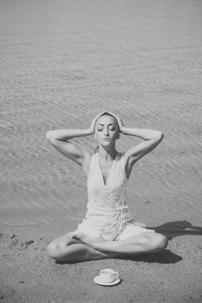 Vrouw mediteren in yoga houding met koffiekopje aan water — Stockfoto