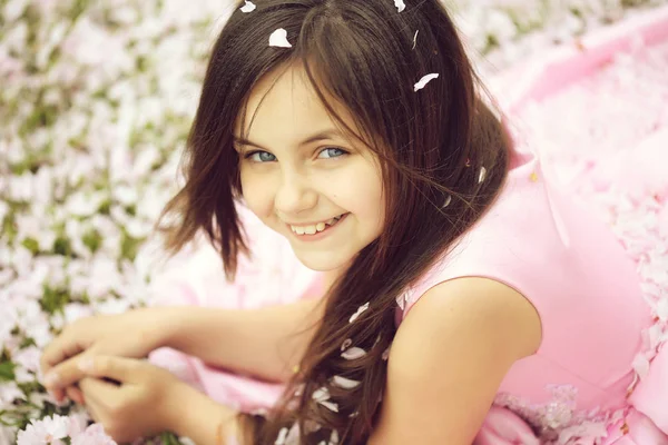 Little girl on green grass with petals — Stock Photo, Image