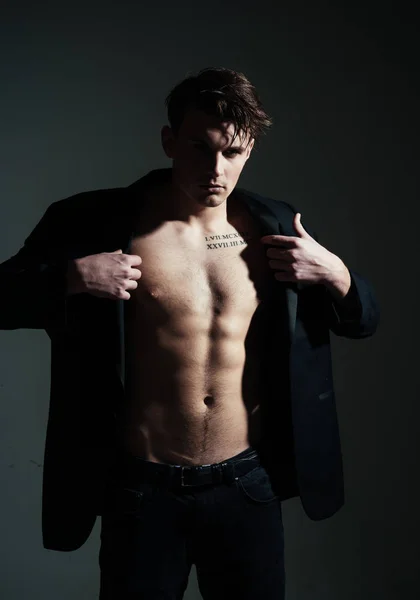 Fashion concept. Macho on pensive face, muscular figure, sportsman, bodybuilder. Guy looks confident and attractive. Man with torso, muscular macho with six packs, dressing jacket, dark background.
