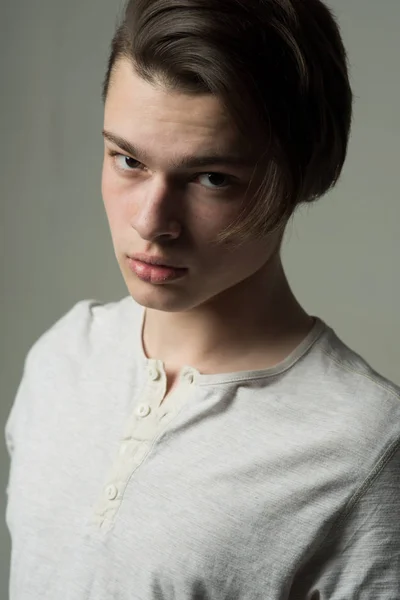 Närbild porträtt av ung man med långt mörkt hår. Självsäkra tonåringen med trendig frisyr i vit T-shirt isolerade på grå bakgrund — Stockfoto