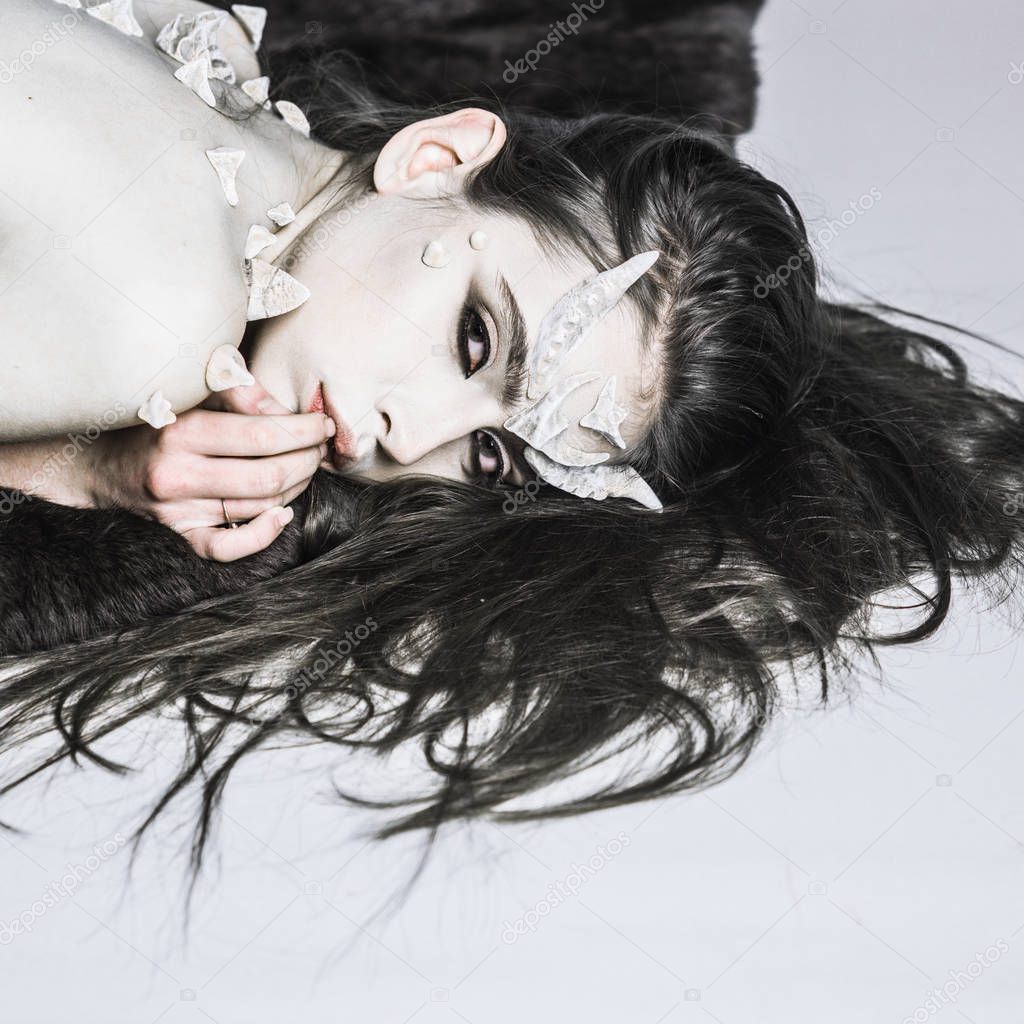Magical horror female creature lay light background. Halloween fictional creature make up long hair. Woman make up demon beast halloween celebrate. Demon with horns and thorns fashionable style