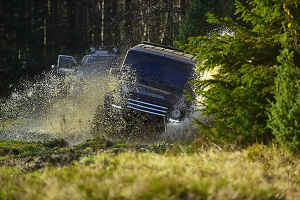 Veicolo utility sportivo o SUV attraversando pozzanghera con spruzzi. Raduno, competizione e quattro ruote motrici concetto. Corse automobilistiche nella foresta autunnale. Offroad gara su sfondo autunno natura — Foto Stock