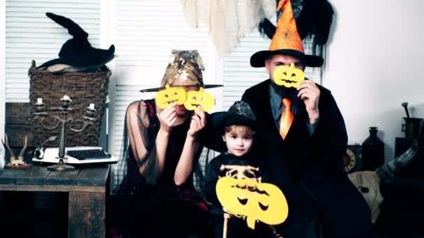 De jongen, zijn vader en moeder in pakken van heksen, skeletten en tovenares, bedekken hun gezicht met meloenen. Familie in kostuums hebben plezier op halloween. — Stockvideo