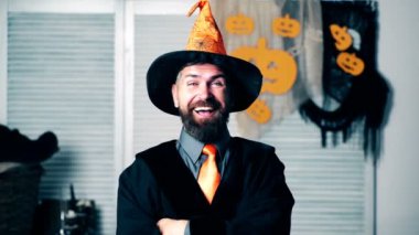 Büyücü turuncu şapkalı içtenlikle gülüyor ve kaşlarını yükseltir. Cadılar Bayramı büyü. Açık yürekli Sihirbazı gülüyor.