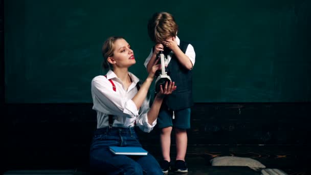 De jongen en zijn moeder kijken naar iets in de microscoop tegen de achtergrond van de klas. Leren concept. Terug naar school. — Stockvideo