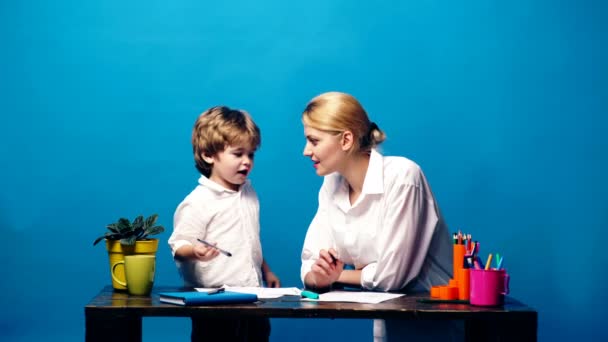 A boy and mother dressed in white shirts communicate and draw on a blue background. — Stock Video