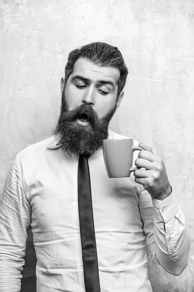 bearded man with curious face look into tea, coffee cup