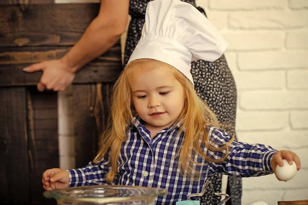 Ребенок в шляпе шеф-повара разбивает яйцо миски на кухне — стоковое фото