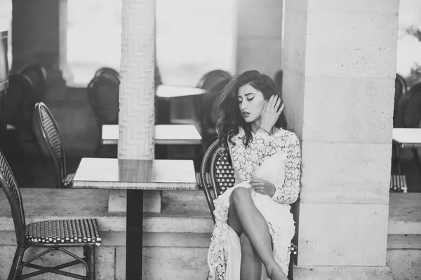 Frau im weißen Kleid im Freien. sexy Frau sitzen allein in Straßencafé. Mode-Modell mit Glamour-Look und Make-up. Mädchen mit langen brünetten Haaren, Schönheit. Braut mit Make-up Gesicht — Stockfoto