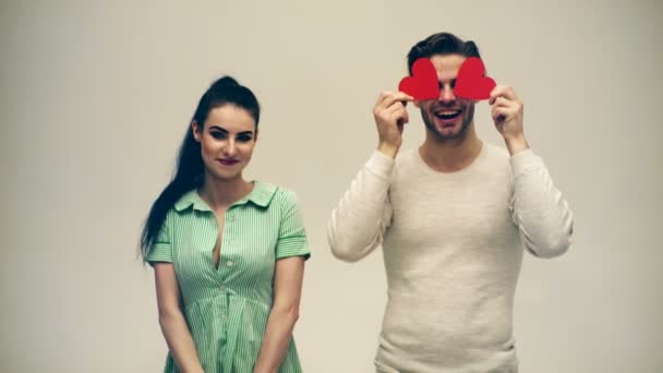 Il ragazzo chiude gli occhi con il cuore e la ragazza si vergogna in piedi accanto a lui su uno sfondo bianco. Il concetto di amore. San Valentino . — Video Stock