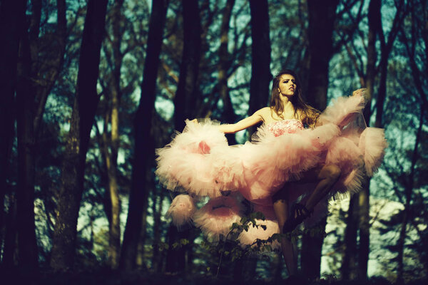 Beautiful young woman in pink glamour dress with long curly hair dancing in sunny forest with blue sky