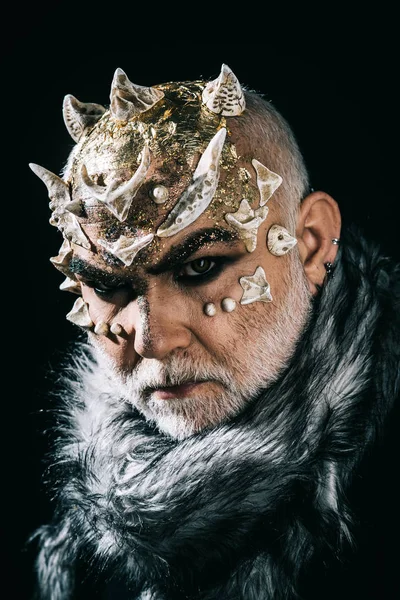 Äldre man med vitt skägg klädd som monster. Demon på svart bakgrund, på nära håll. Man med törnen eller vårtor i päls. Teatraliska makeup koncept. Främmande, demon, trollkarl makeup. — Stockfoto