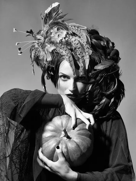 Красивая женщина в шляпе из перьев держит тыкву на Хэллоуин — стоковое фото