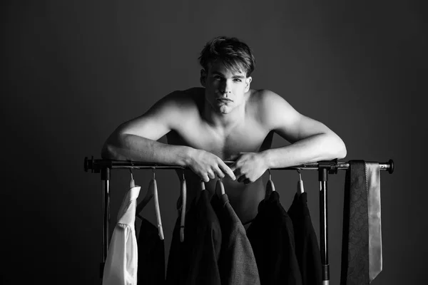 shaved man with naked muscular torso standing at wardrobe hanger