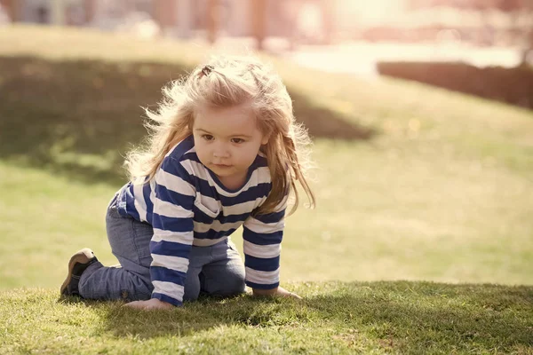 Yeşil çimenlerin üzerinde oturan uzun sarı saçlı çocuk