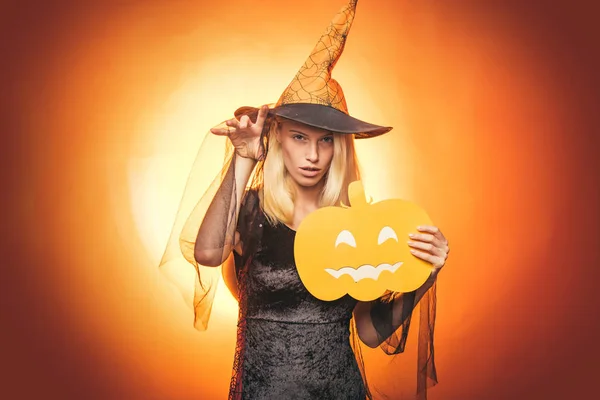 Halloween kleding en kostuums en heks hoeden van de heks. Vrolijke Halloween. Gelukkig lachende vrouw op een oranje achtergrond. Gelukkig Stickers. Halloween heks met gebeeldhouwde pompoen. magische verlichting in donkere bos — Stockfoto