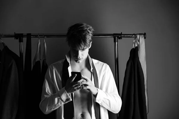 Guy with muscular torso at wardrobe hanger with phone — Stock Photo, Image
