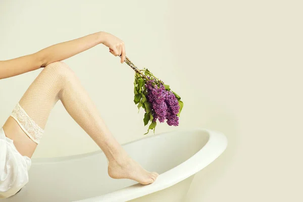 Hand with lilac and leg on bathtub — Stock Photo, Image