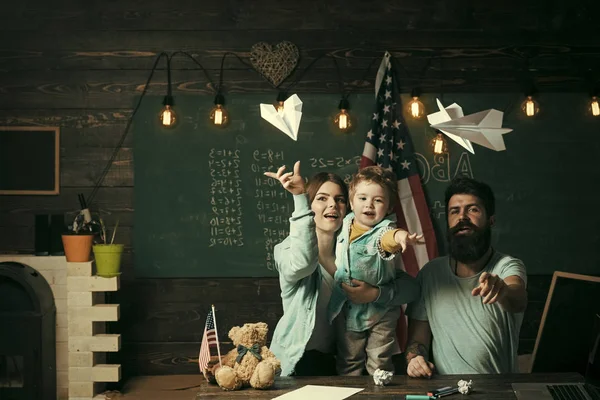 American family at desk with son play with paper planes. Homeschooling concept. Kid with parents in classroom with usa flag, chalkboard on background. Parents teaching son american traditions playing. — Stock Photo, Image