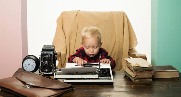 Маленька дитина друкує папір на ретро друкарській машинці за столом. Хлопчик набирає ключі на старовинній машині — стокове фото