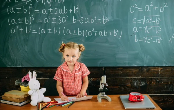 Flicka ritning på svarta tavlan bakgrund. Liten flicka på lärare skrivbord i skolklass. En konst som infunderas skola — Stockfoto