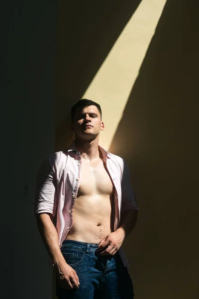 El hombre de camisa abierta muestra un torso sexy. Modelo hombre con mirada seria de la cara en la pared soleada —  Fotos de Stock