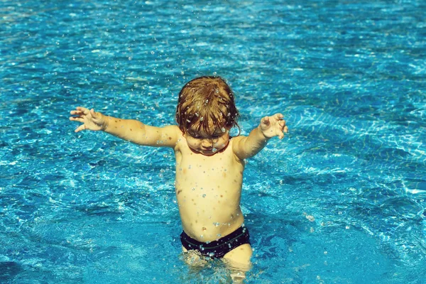 Netter kleiner Junge mit nassen Haaren bestreut Wasser im Pool — Stockfoto
