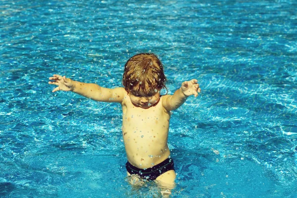 Cute baby boy with wet hair sprinkles water in pool — Stock Photo, Image