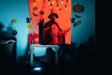 Cadılar Bayramı elbiseleri, cadı kostümleri ve cadı şapkaları. Sihirli şapka. Cadılar Bayramı için en iyi fikir. Balkabağı fenerleri. Cadılar Bayramı arka planında sihirli kitapla mutlu bir baba. Sihirli balkabağı. İnsan Korku Yüzleri.