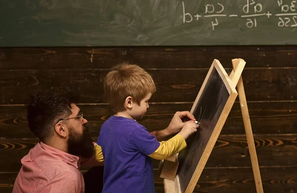 Studente vista laterale e insegnante di fronte alla lavagna. Padre o tutor aiutano il bambino a scrivere lettere. Uomo e bambino su pannelli di legno sfondo — Foto Stock