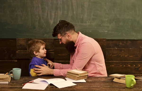 Male teacher explaining something to the boy. Side view bearded man in glasses and blond child in front of green board. Teacher holding naughty kid — Stock Photo, Image