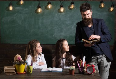 Öğretmen ve kız öğrencilerin sınıfta, kara tahta arka plan. İlköğretim Okulu kavramı. Sakallı adam kız öğrenciler, kitap okuma öğretir. Meraklı sakin çocuklar öğretmen dikkat ile dinleme.