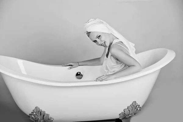 Kvinna med handduk turban sitter i vita badkar — Stockfoto