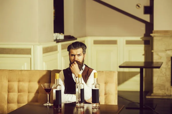 Hipster sentado en el sofá con vaso de martini y tres botellas — Foto de Stock