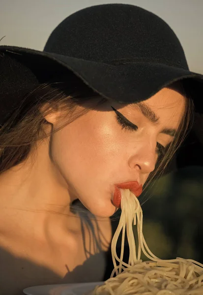 Bonita imagen de una hermosa mujer comiendo pasta en sombrero negro —  Fotos de Stock