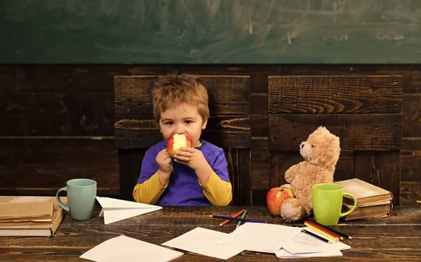 School break. Hungry kid eating apple in classroom. Small boy playing with paper plane