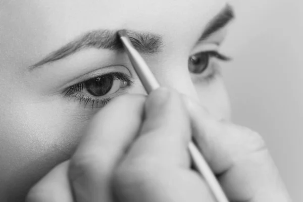 Mulher com olhos azuis recebendo maquiagem nas sobrancelhas — Fotografia de Stock