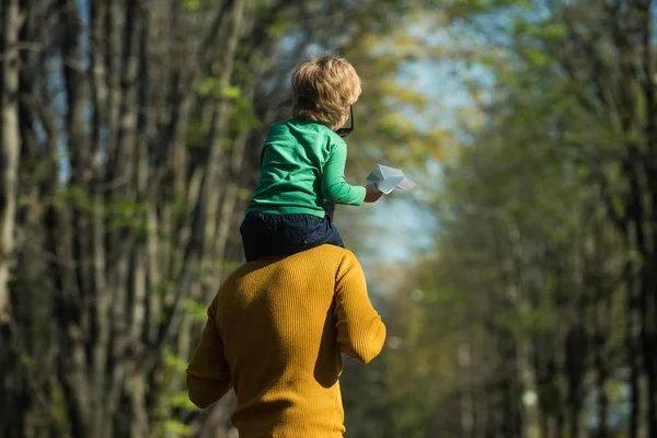 Passeio de volta. Pai segure pequeno filho em ombros dando criança piggyback no parque. Relaxa, estás comigo. — Fotografia de Stock