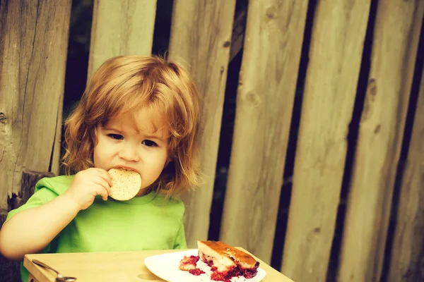 Kleine jongen eten taart in de buurt van houten hek — Stockfoto