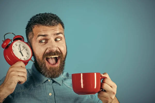 Hombre con barba en cara feliz con taza, despertador — Foto de Stock