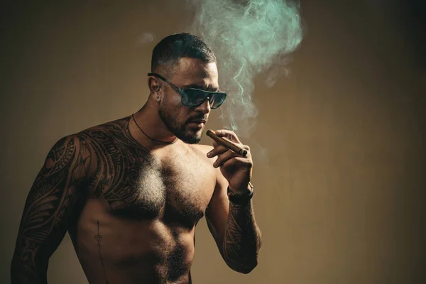 Tattooed man met sigaar. Sigaar roken genieten van leven en moment. Portret van een bebaarde zakenman met een mooie torso een sigaar roken en het drinken van whisky. Cubaanse sigaren. Kopiëren van ruimte — Stockfoto