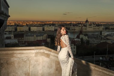 Şehvetli kadın balkonda, güzellik uzun saçlı. Şehir Manzaralı, moda akşam üzerinde beyaz gelinlik kadın. Gelin makyaj ile. Moda modeli stil ve saç modeli. Kız glamour bakışla