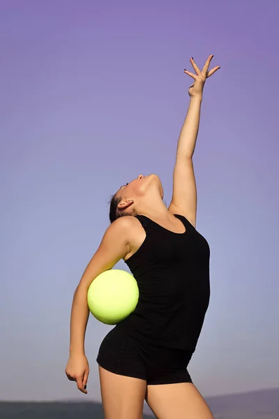Woman gymnast in black sportswear with green ball.