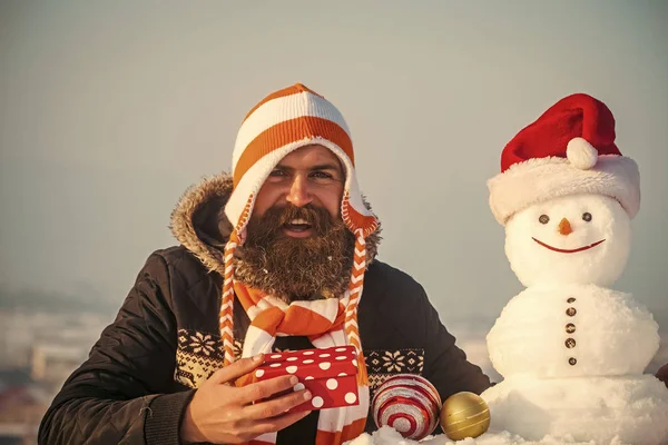 Хіпстер в капелюсі посміхається зі сніговиком в шапці Санта — стокове фото