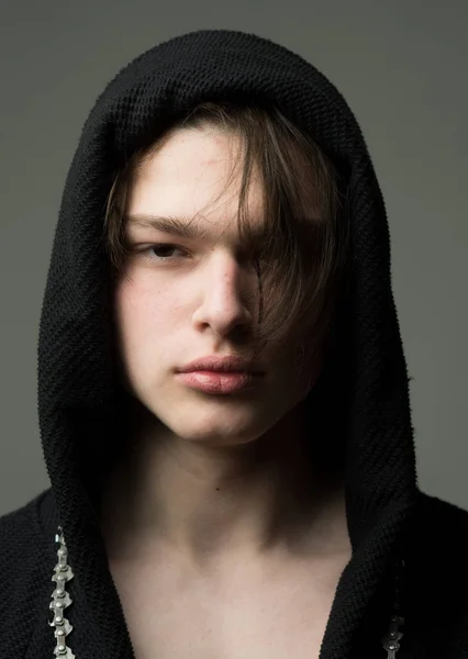 Tipo con cara confiada en capucha negra, fondo gris. Macho en albornoz negro con capucha, de cerca. Concepto masculinidad. Hombre con la piel lisa en la cara y el cuello mirando a la cámara . — Foto de Stock