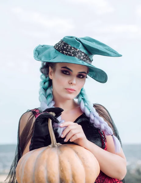 Mulher posando com abóbora. Bruxa de Halloween com um chapéu mágico. Bela jovem mulher surpreso em chapéu de bruxas e traje segurando abóbora. Menina modelo atraente em traje de Halloween . — Fotografia de Stock
