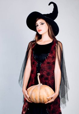 Cadı kostümlü göz kamaştırıcı vampir. Balkabağıyla poz veren kadın. Cadıların şapkası ve kostümü içinde balkabağı tutan genç ve güzel bir kadın..