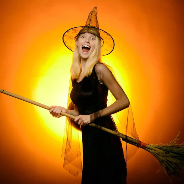 Surprised woman on witches hat and costume with broom. Vampire Halloween Woman portrait. Emotional young women on halloween party over red background. Looking camera.